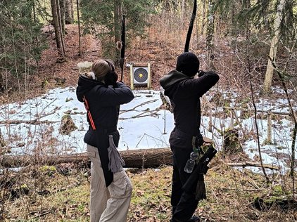 Zwei Kinder zielen mit Bögen auf eine Zielscheibe im Wald